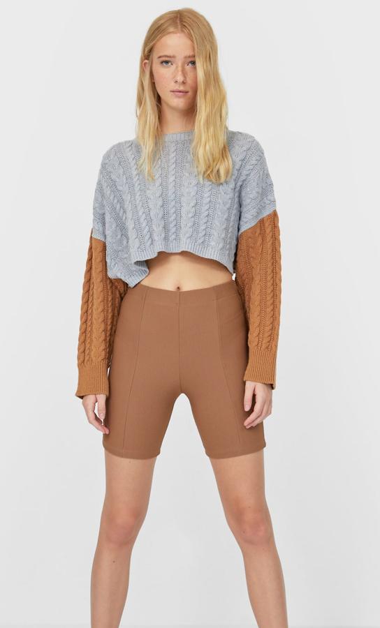 En gris y marrón, este jersey corto de tejido trenzado y cuello redondo tiene un precio de 19,99 euros.