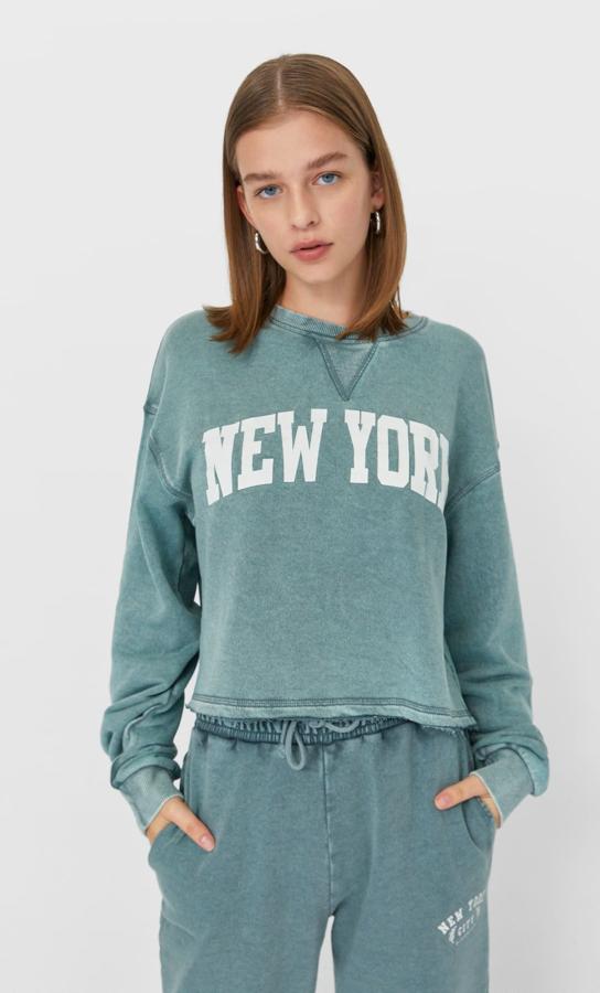 En verde degradado, con estampado de letras a contraste, cuello redondo y mangas largas, esta sudadera crop de Stradivarius viene con bajo acabado sin costura y mangas acabadas en puño. Cuesta 15,99 euros y podemos encontrarla entre las tallas XS y L.