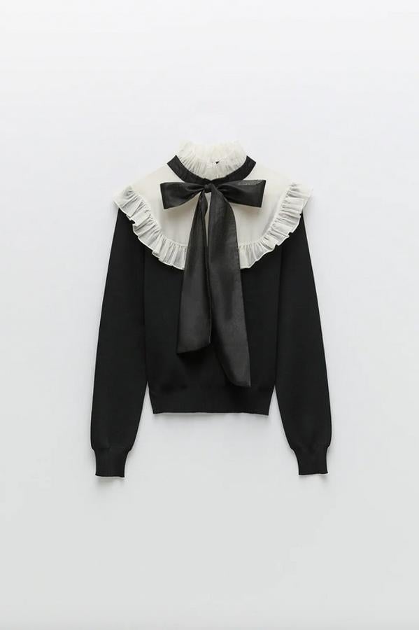 Cuello subido con lazo y mangas largas para este jersey negro de Zara con tejido combinado a contraste en el pecho y los hombros confeccionado en organza con volantes. Solo queda en las tallas S y M por 25,95 euros.