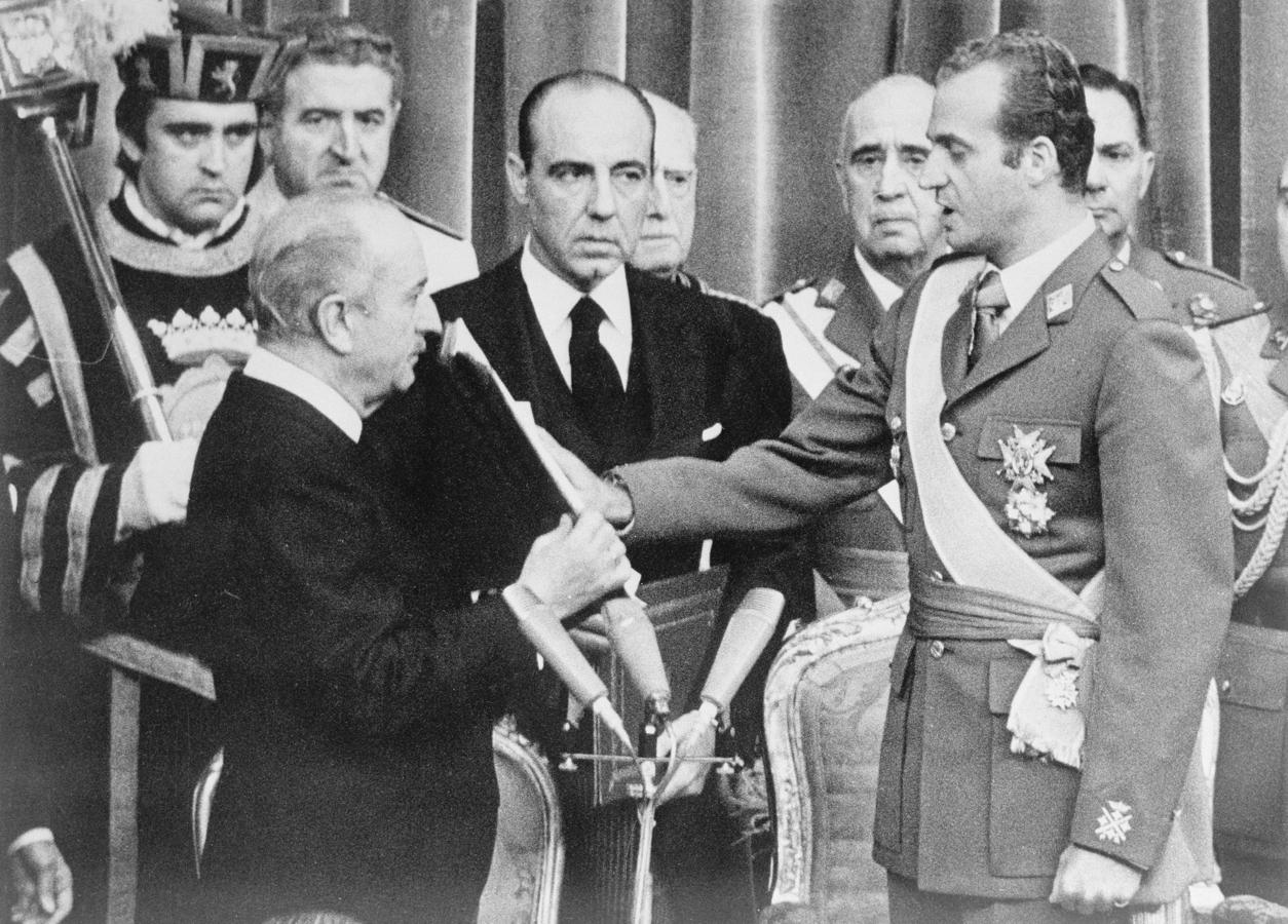 Con el cadáver Franco aún de cuerpo presente, don Juan Carlos fue proclamado Rey de España, jurando ante la Biblia los principios del Movimiento (imagen). Llevaba años preparándose para este momento y, sin que el Caudillo lo supiera, también preparando todo para una Transición ejemplar que acabara con la Dictadura y el Franquismo y diera paso a una democracia en forma de Monarquia Parlamentaria. Lo hizo, como definió su consejero y Presidente de las Cortes Torcuato Fernández Miranda "de la ley a la ley, a través de la ley".