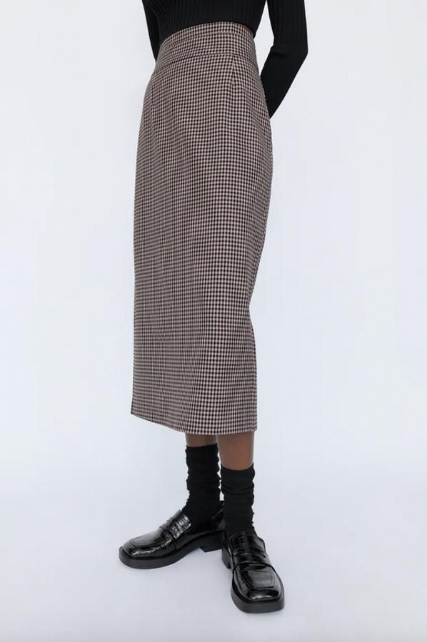 Confeccionada con al menos un 25% de poliéster reciclado, esta falda de cuadros de Zara en rosa palo y negro es de tiro alto y viene con abertura en el bajo en la parte posterior. Cuesta 25,95 euros y está disponible entre las tallas XS y L.