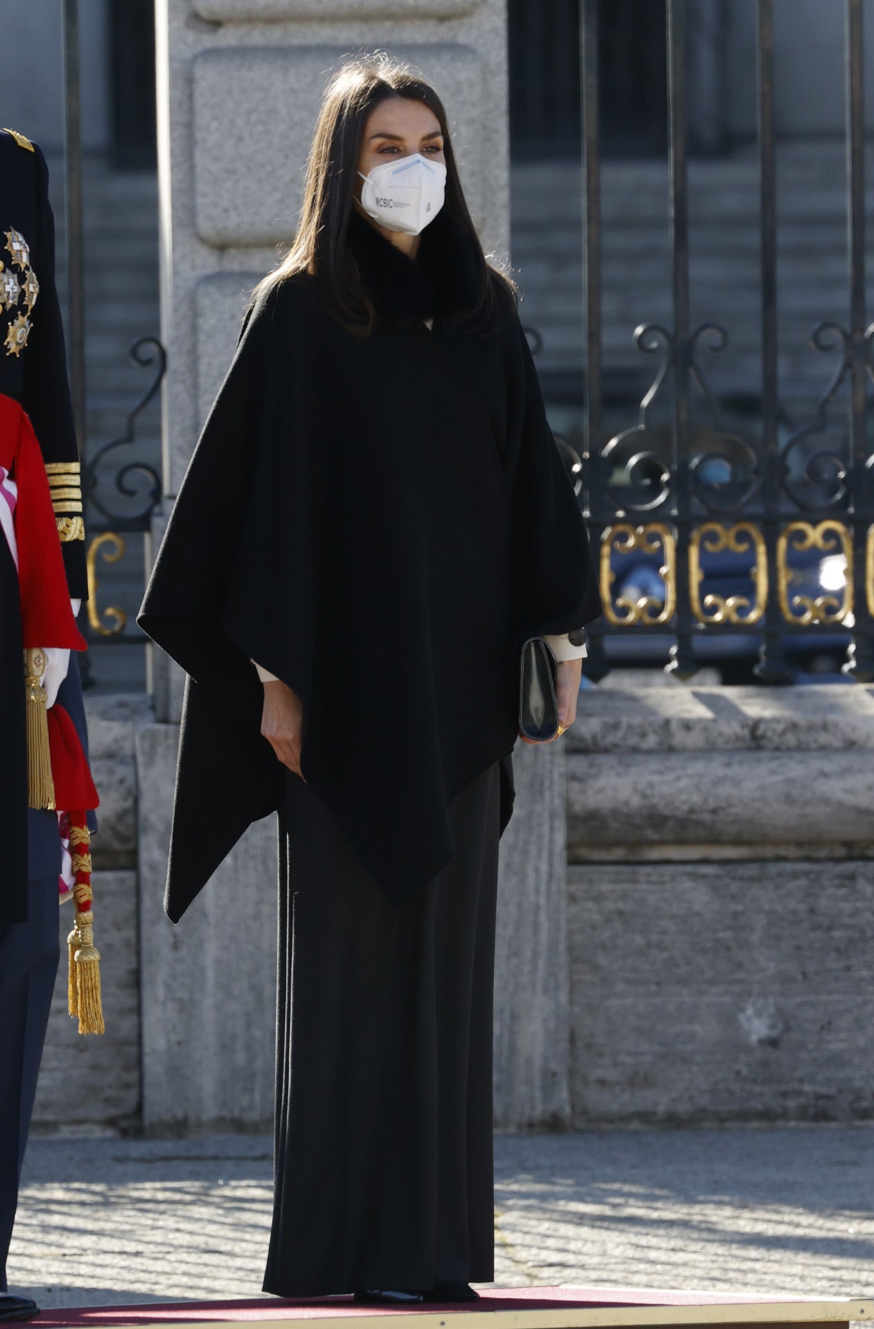 Para este 6 de enero de 2021, doña Letizia ha llevado uno de sus looks más sobrios que le recordamos en la Pascua Militar: un look 'black&white' que combinaba una sencilla falda larga negra con una original blusa blanca con detalle de volante vertical y grandes botones en contraste, una pieza nueva de  la firma española Maksu  que supone el primer estreno de la Reina en meses. Para protegerse de las bajas temperaturas, la Reina recuperó su capa de Carolina Herrera. Como complementos, sus salones de tiras cruzadas de Magrit y un clutch joya de Felipe Varela.