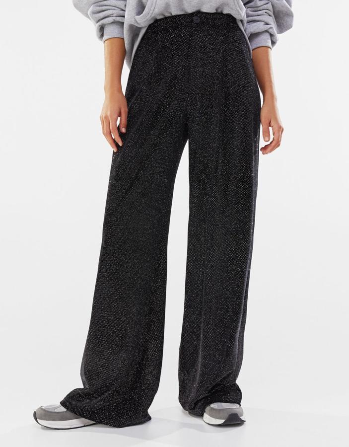 En terciopelo con brillos plateados, estos pantalones de pernera ancha de Bershka en color negro con cierre de cremallera y botón ha pasado de 29,99 euros a 17,99 euros y está disponible entre las tallas XS y L.