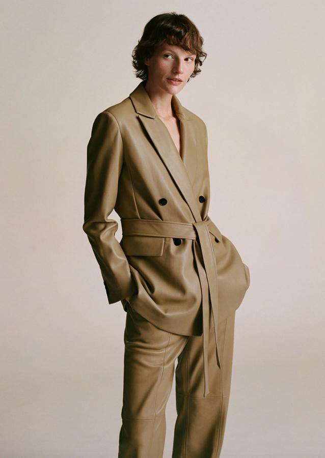 En color oliva y efecto piel, esta americana de diseño recto estructurado y cruzado es de Mango y viene con cuello de solapa, mangas largas con puños abotonados y cinturón a tono desmontable. Con bolsillos laterales de solapa y cierre de botones a contraste en el frontal, cuesta 59,99 euros y está disponible entre las tallas XS y XL.