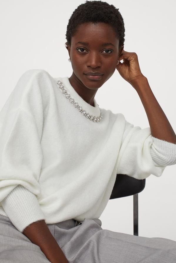 En punto suave con lana en la trama y remaches decorativos, este jersey blanco de H&M con escote redondo, hombros caídos y mangas amplias viene con remate de canalé en el cuello, puños y bajo. Podemos encontrarlo entre las tallas XS y XL por 19,99 euros.