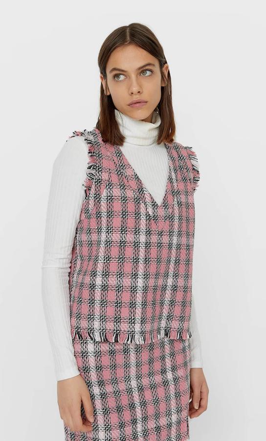 Con cuello de pico y manga sisa desflecada, al igual que el bajo, este chaleco en rosa chicle, negro y blanco con estampado de cuadros está disponible entre las tallas XS y XL por 17,99 euros.