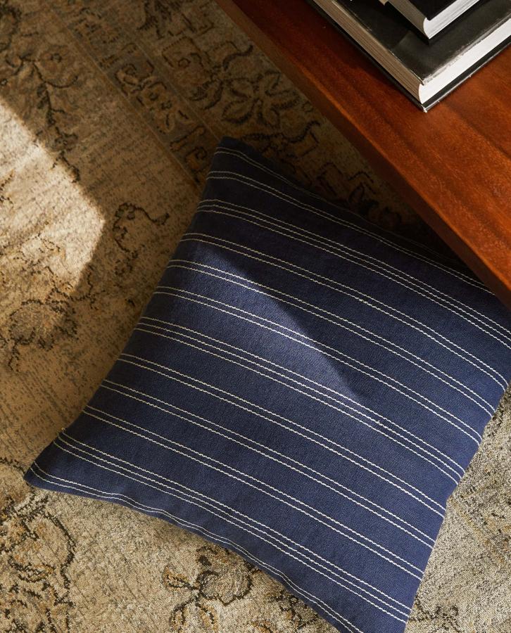Disponible en azul, amarillo y blanco roso, esta funda de cojín de lino con rayas mide 45x45 centímetros y tiene un precio de 9,99 euros.