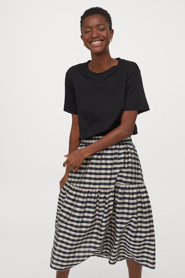Con estampado de cuadros negros sobre fondo blanco, esta falda de H&M en mezcla de modal y lyocell es de talle alto con diseño midi, elástico revestido en la cintura y costura fruncisa para dar vuelo. Tiene un precio de 29,99 euros y podemos encontrarla entre las tallas XS y XXL.