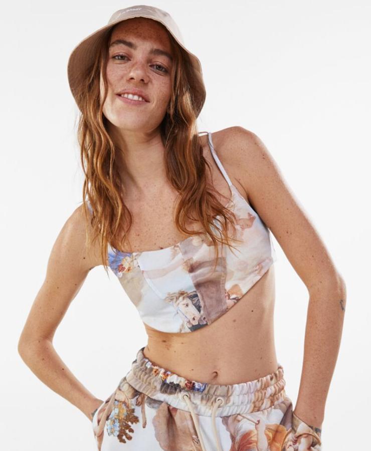 Top muy corto de tirantes finos y estampado de pintura renacentista. Puede llevarse a conjunto con un pantalón de chándal y goma elástica en la cintura y sudadera ancha con capucha con el mismo print. Su precio es de 15,99 euros, el del pantalón 25,99 euros y el de la sudadera 29,99 euros.