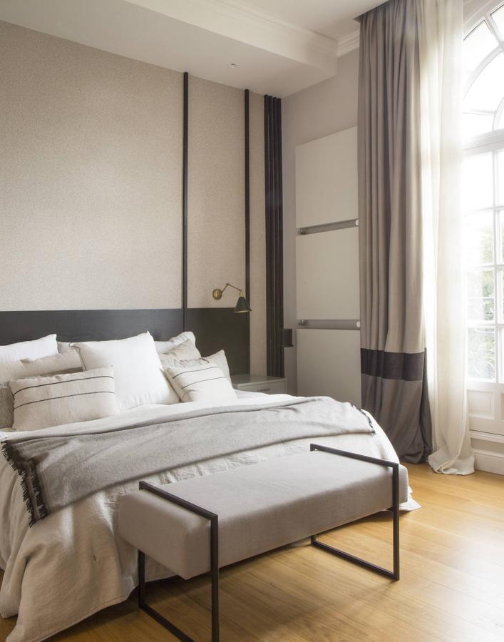 La suite principal tiene forma de hache. El cabecero y la banqueta son diseño de la interiorista. El papel de la pared es de La Maison Barcelona y el aplique, de Luz Vintage.