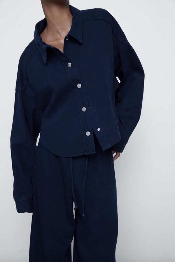 En azul marino, con cuello solapa y manga larga acabada en puño, esta camisa crop de Zara con bajo asimétrico y cierre frontal de botones metalizados podemos encontrarla entre las tallas XS y XXL por 25,95 euros.