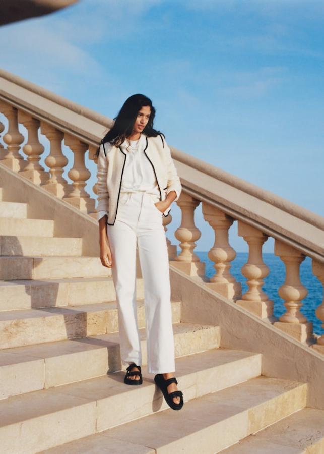 Look de la nueva colección de Mango con chaqueta corta bicolor, pantalón "mom" de color blanco y sandalias trenzadas.
