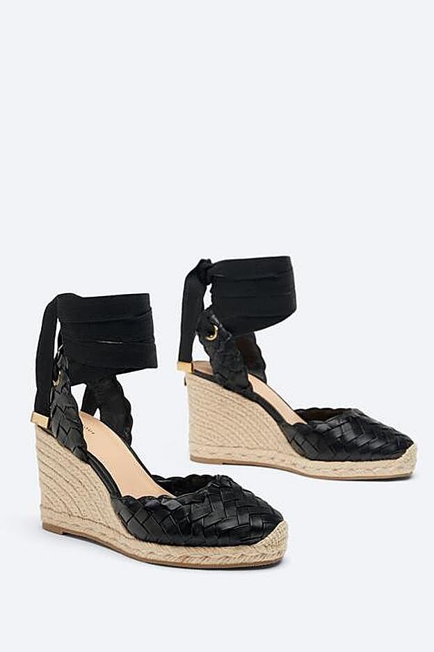 Fabricada en piel ovina trenzada, esta cuña de color negro tiene una altura de 10 centímetros.