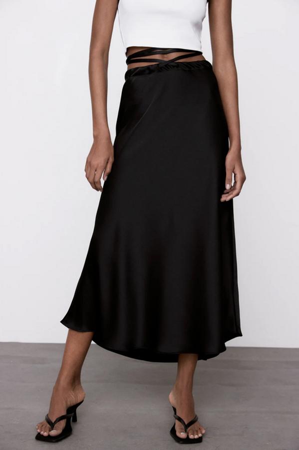 Con detalle de cintas cruzadas en la cintura, esta falda negra de diseño midi, tiro alto y bajo con vuelo es de Zara y tiene un precio de 25,95 euros. Está disponible entre las tallas XS y XL.