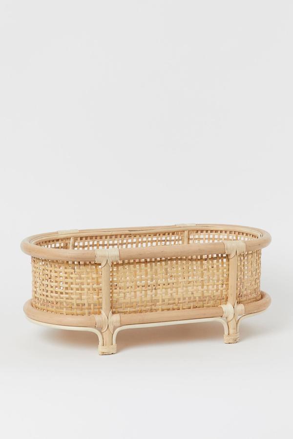 Este macetero bajo con forma ovalada en ratán trenzado con marco fijo y patas tiene una altura de 22 centímetros y un ancho de 54. Su precio es de 39,99 euros.