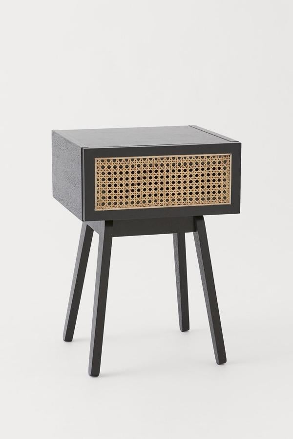 Esta mesita de noche en madera de color negro y cajón con frente de ratán tiene un ancho de 35 centímetros, una altura de 58 y un largo de 35. Su precio es de 129 euros.