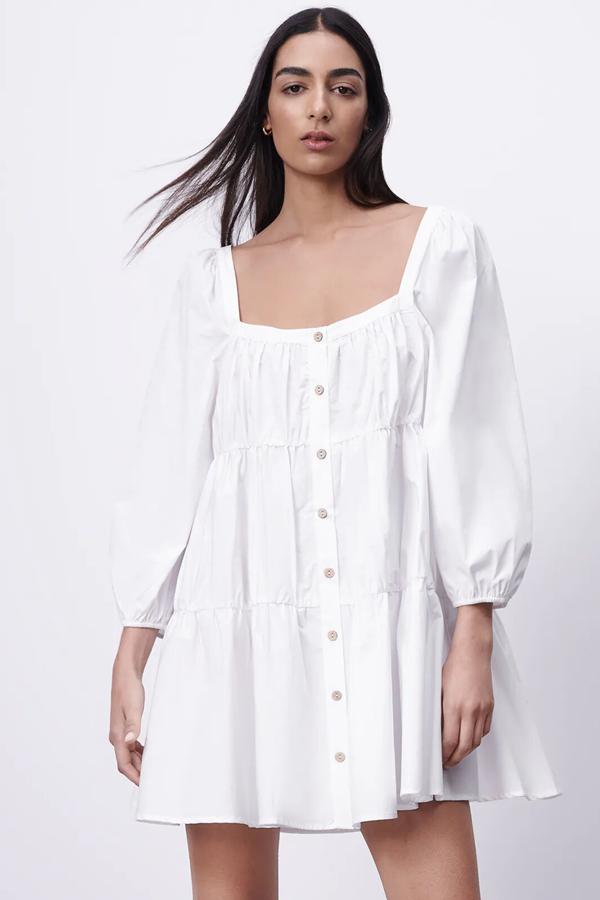 Este vestido blanco de corte mini y con escote recto cuenta con manga larga acabada en elástico y cierre frontal con botones. Es de Zara y tiene un precio de 29,95 euros.