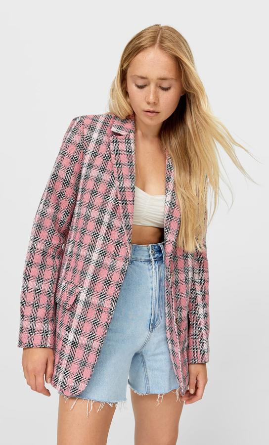 Con cuadros en color rosa chicle, esta blazer con manga larga acabada en botón y hombros marcados cuenta con cierre mediante botones metálicos y tiene un precio de 39,99 euros. Es de Stradivarius.