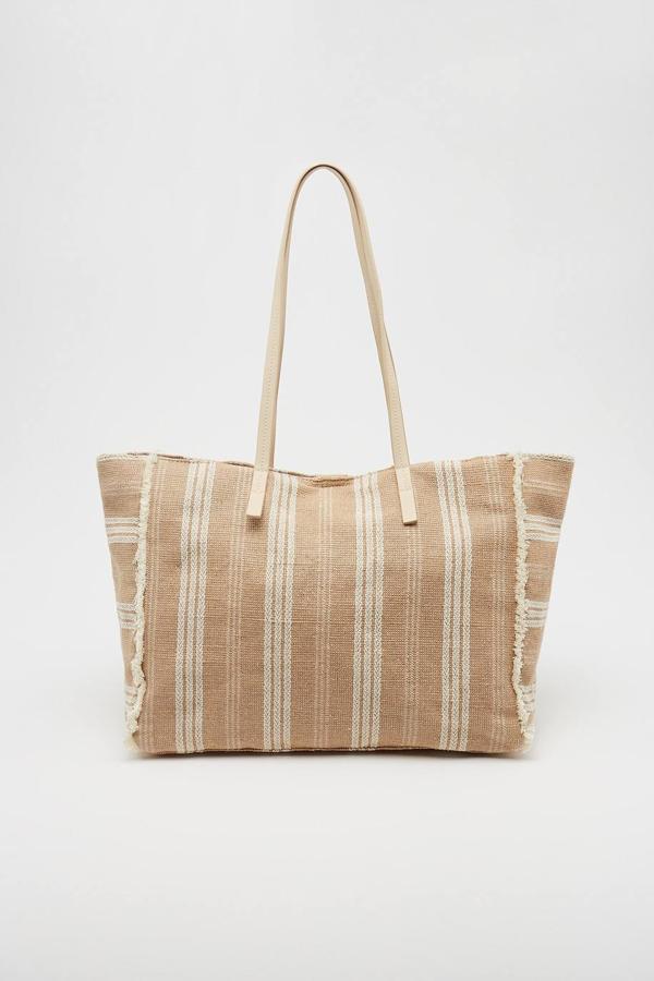 El verano aún queda lejos, pero si quieres adelantarte y darle un aire playero a tu look, elije esta bolsa rústica de rafia con detalle de flecos. Tiene doble asa y puede ser tuya por 17,99 €.