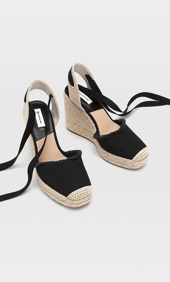 Con una altura de 11 centímetros, estas cuñas negras de yute con cierre de tiras atadas al tobillo tienen un precio de 29,99 euros.