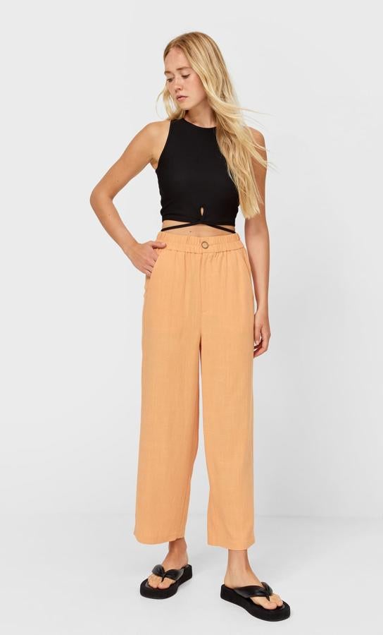 En color naranja melocotón, este pantalón fluido de tiro alto y pernera ancha cuenta con bolsillos delanteros y tiene un precio de 19,99 euros.