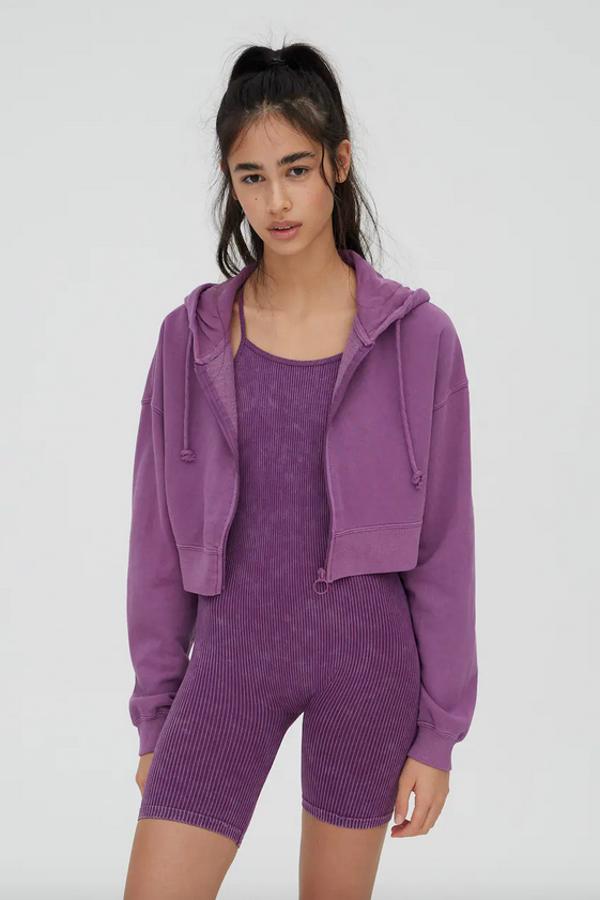 Disponible en violeta, marrón claro y lima, esta sudadera cropped de Pull&Bear con cierre de cremallera frontal y capucha con cordón a tono tiene un precio de 17,99 euros y podemos encontrarla en las tallas S, M y L.