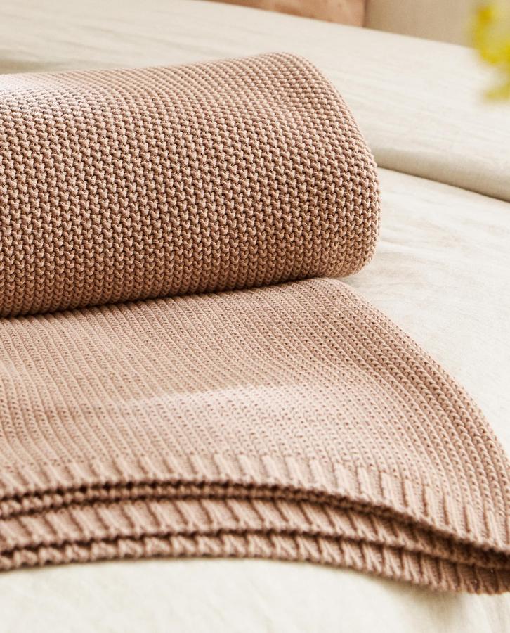 Esta manta de punto de algodón con diseño geométrico en los bordes mide 140x190 centímetros y está disponible en varios colores. Tiene un precio de 49,99 euros.