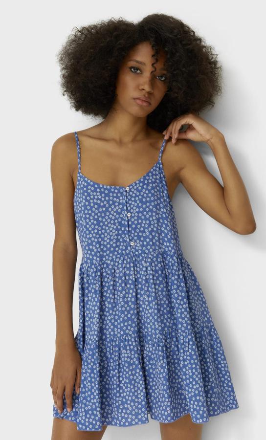 Este vestido corto con escote recto y tirante fino cuenta con volantes en el bajo y detalle de botones en la parte delantera. En color azul con estampado de margaritas, tiene un precio de 19,99 euros.