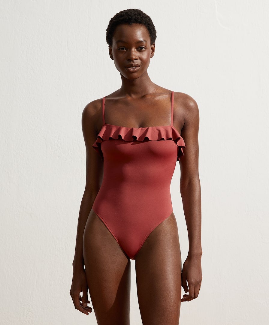 Bañador rosa de Oysho con escote recto y detalle de volantes, copa extraíble sin aro y tirantes ajustables. Tejido con poliamida reciclada. (29,99 euros).