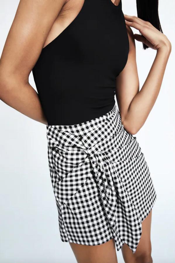 De tiro alto, con detalle de nudo delantero y cierre lateral con cremallera oculta en costura, esta falda pantalón de Zara con estampado de cuadro vichy en blanco y en negro cuesta 25,95 euros y está disponible en las tallas XS, S y M.