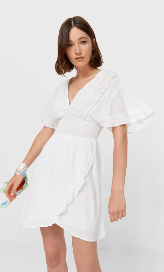 Este vestido de color crudo con escote de pico y manga corta con volante cuenta con gomas en la cintura y tiene un precio de 29,99 euros. Es de Stradivarius.