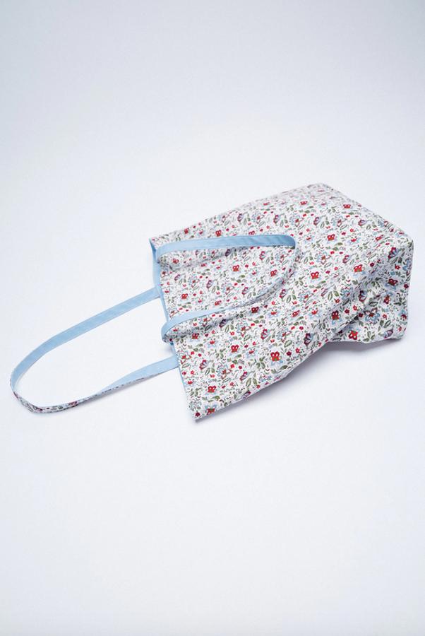 Este bolso shopper de Zara confeccionado con al menos un 25% de poliéster reciclado es reversible y por un lado el cuerpo es en azul cielo y por otro con estampado de flores en azul, caqui, blanco y rojo. Cuesta 19,95 euros.