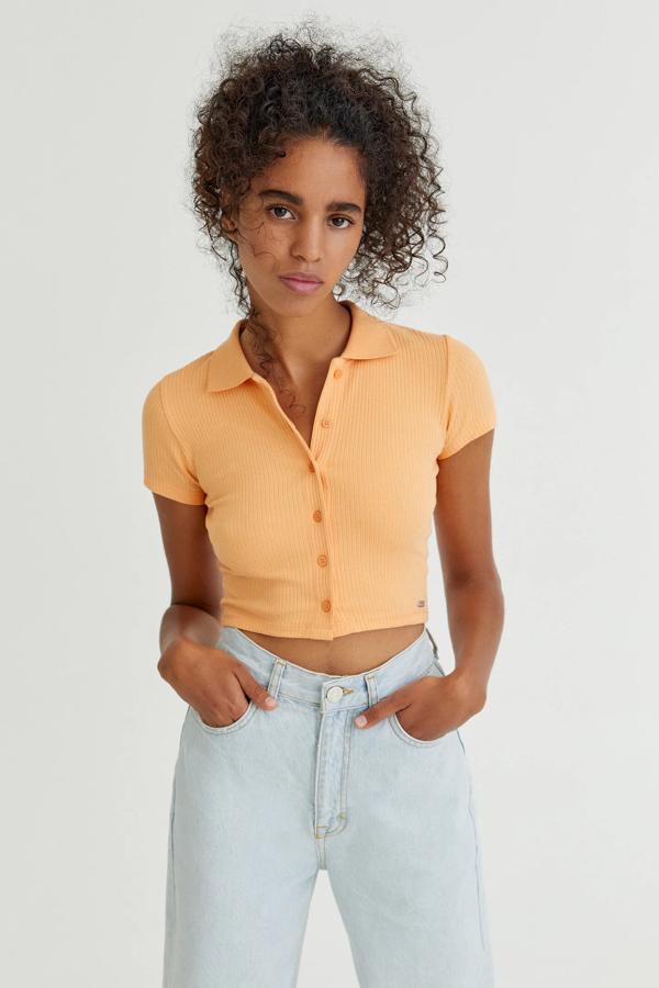 Esta camiseta tipo polo en color naranja cuenta con cierre de botones delanteros y tiene un precio de 9,99 euros.