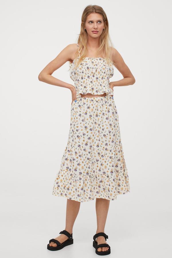 En color crema con estampado de flores lilas y naranjas, esta falda midi vaporosa de H&M con elástico revestido en la cintura viene con diseño fruncido escalonado y abertura pronunciada en el frontal. Cuesta 19,99 euros y está disponible entre las tallas 32 y 50.