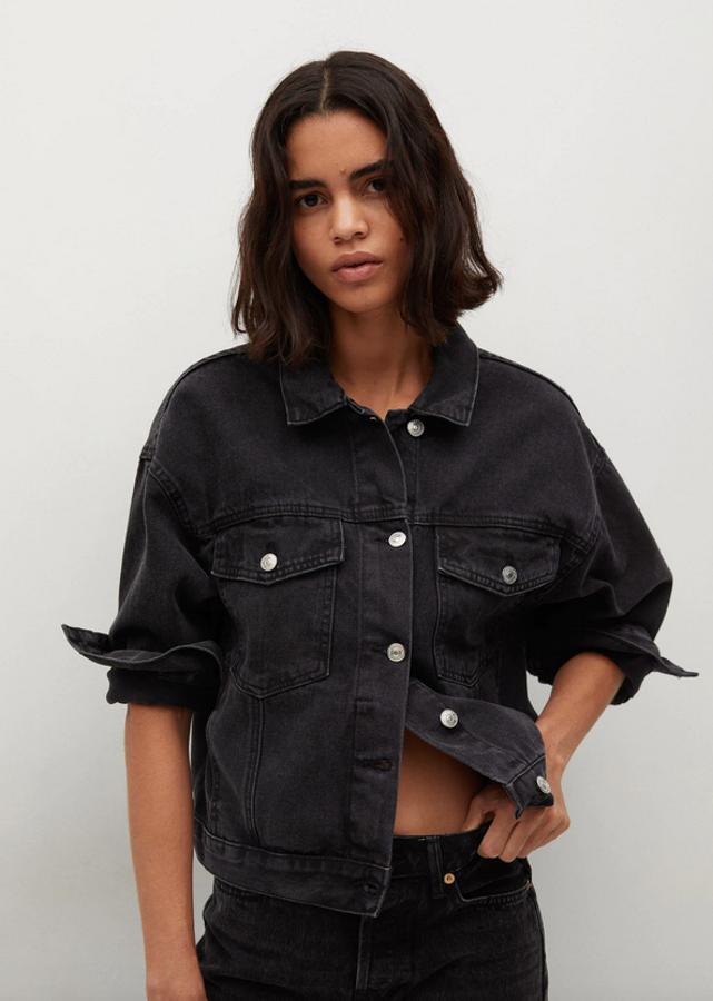 En color negro, con diseño oversize, cuello de solapa y mangas largas con puños abotonados, esta cazadora vaquera de Mango viene con dos bolsillos de solapa en el pecho y cierre de botones metálicos frontal. Disponible entre las tallas XS y XL, cuesta 29,99 euros.