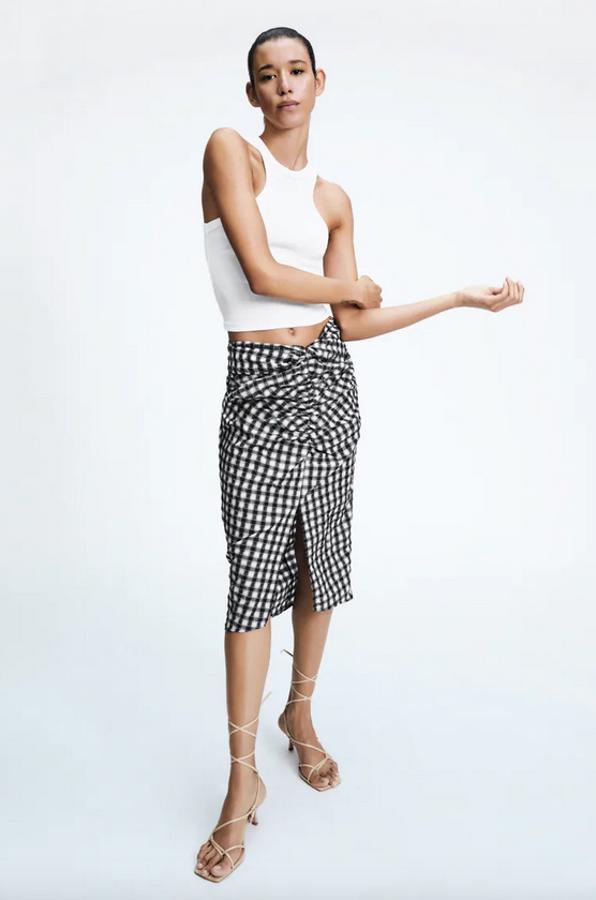 Estampado de cuadros blancos y negros para esta falda midi de tiro alto con detalle de nudo delantero, bajo con abertura frontal y cierre en la espalda con cremallera oculta en costura. Podemos encontrarla entre las tallas XS y XL por 22,95 euros.
