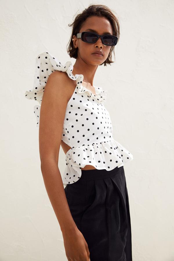 Este top en color blanco con lunares negros cuenta con un escote de pico profundo y ribete de volante y espalda descubierta con tiras finas transversales. Tiene un precio de 29,99 euros.