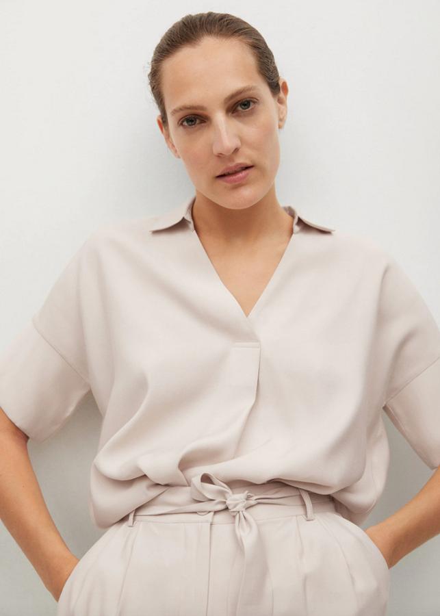 En color beige, confeccionada en tejido fluido, con escote de pico y cuello de solapa, esta blusa con costura de hombro caída cuesta 25,99 euros y está disponible entre las tallas XS y L.