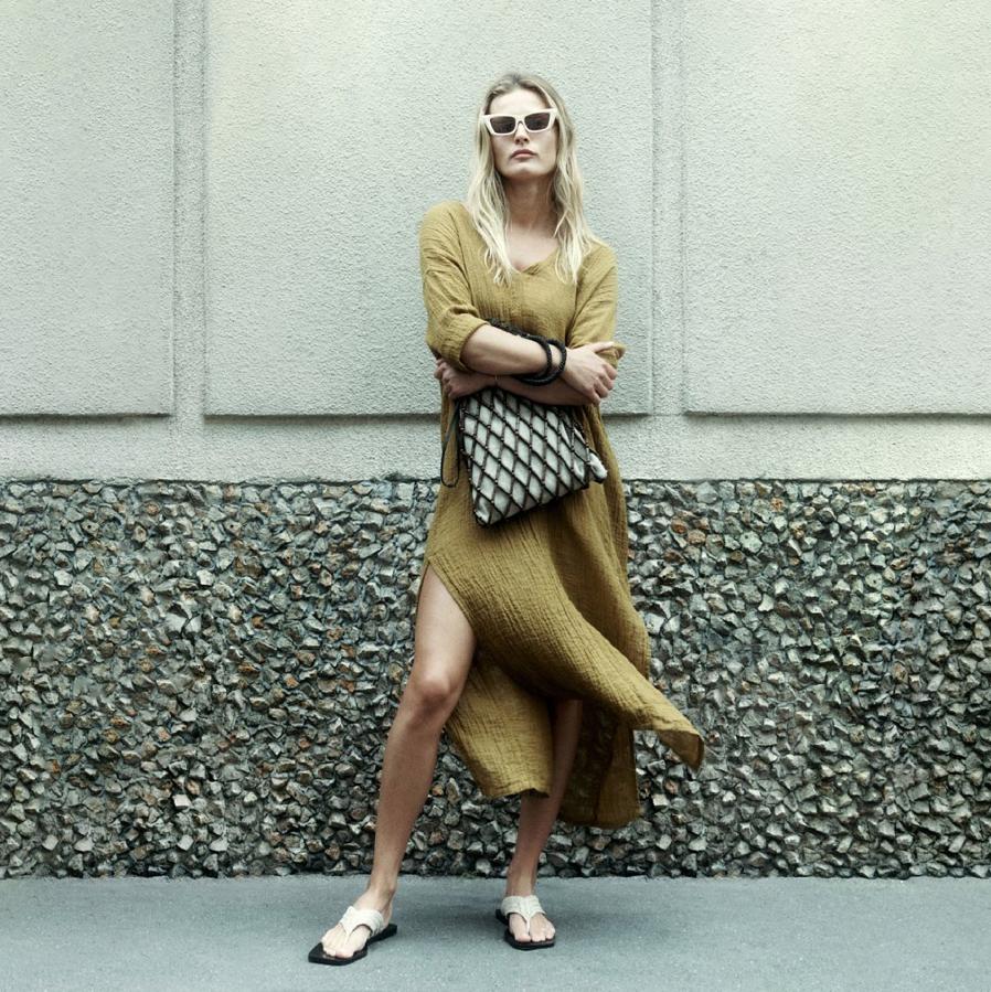 En color aceite, con aberturas laterales en el bajo recto y corte fluido, este vestido de lino con cuello de pico tiene un precio de 99,95 euros y está disponible en las tallas XS-S y M-L.