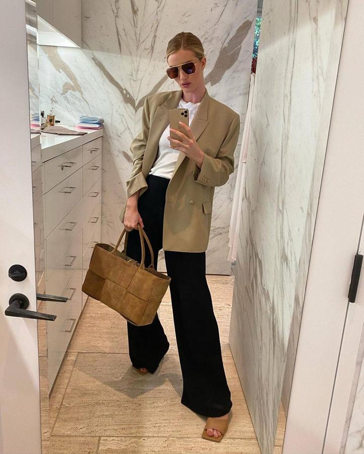 La modelo propone un look compuesto por blazer 'oversize' beige, camiseta básica blanca, pantalón de pata ancha negro, 'mules' camel de tacón y bolso grande de piel vuelta.