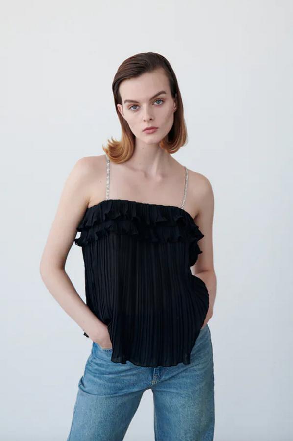 Diseño plisado con escote recto elástico y volantes en el pecho para este top lencero de Zara con detalle de tirantes finos con aplicación joya. Disponible entre las tallas XS y XL, tiene un precio de 22,95 euros. 