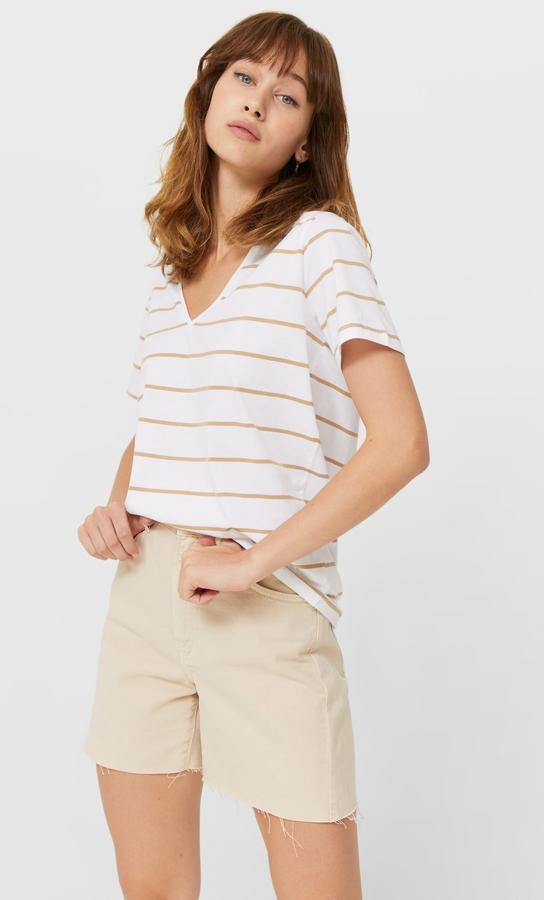 En color blanco con rayas en beige, esta bonita camiseta de Stradivarius con cuello de pico y mangas cortas cuesta 5,99 euros y está disponible entre las tallas XS y XL.