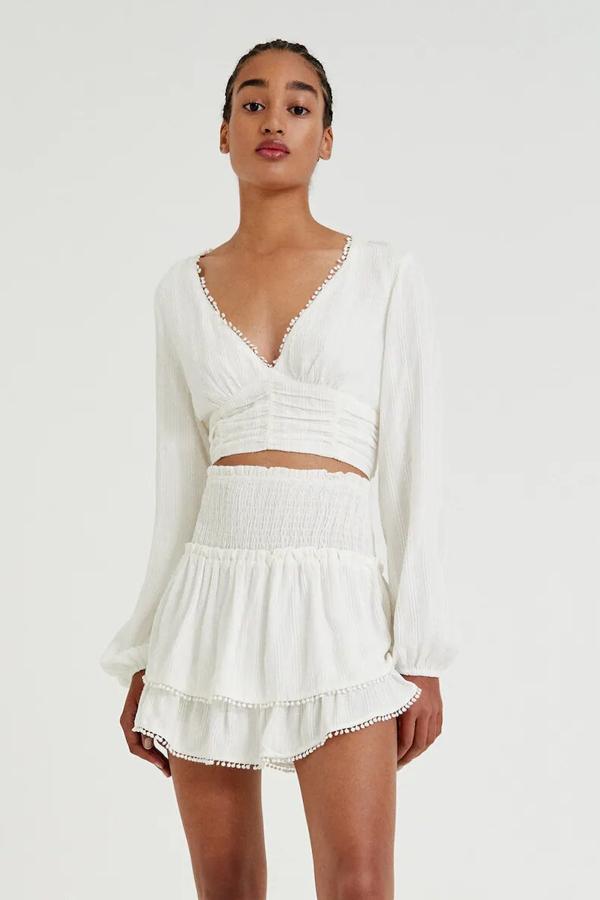 Este conjunto de color blanco está formado por blusa (19,99 euros) de manga larga con puntilla y minifalda (19,99 euros) con volantes a juego.