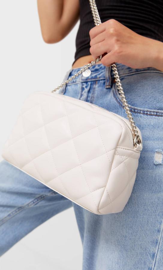 Con abertura superior de cremallera, esta bandolera acolchada en color blanco tiene una única asa larga en cadena y tejido a tono. Cuesta 12,99 euros. 