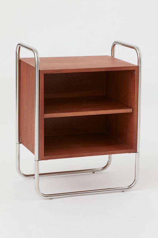 En madera de acacia color marrón, esta mesita de noche con estructura de metal tiene un alto de 66,5 centímetros, un largo de 25 y una profundidad de 35. Su precio es de 179 euros.