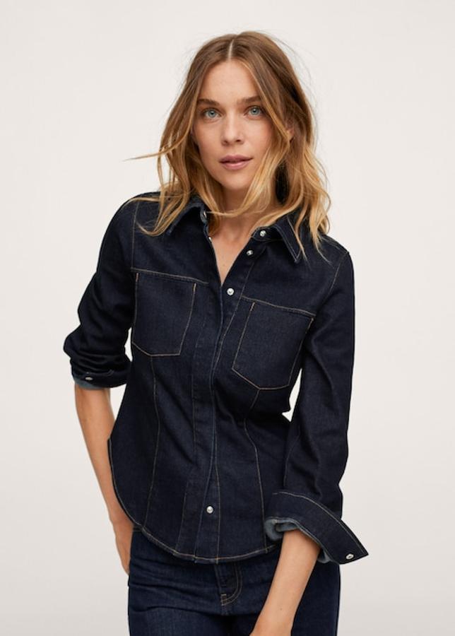 Una de nuestras favoritas es esta camisa de diseño entallado de Mango confeccionada en algodón estilo denim, con cuello clásico y dos bolsillos de plastrón en la pechera. Con costuras vistas a contraste y aberturas laterales en el bajo redondeado, viene con cierre de botones a presión en el frontal oculto por tapeta. Podemos encontrarla entre las tallas XS y XL por 39,99 euros. 