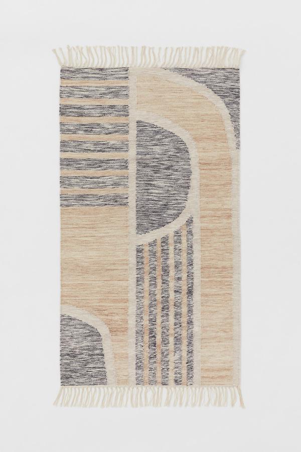 En color beige y con estampado gris, esta alfombra en mezcla de lana y algodón tiene flecos en los extremos y un precio de 69,99 euros. Mide 80x140 centímetros.