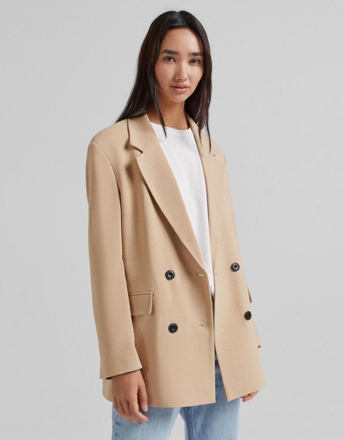 En color camel, con doble botonadura frontal a contraste en negro, bolsillos de solapa y cuello de solapa con muesca, esta blazer de Bershka de corte masculino cuesta 35,99 euros y está disponible entre las tallas XS y L. 