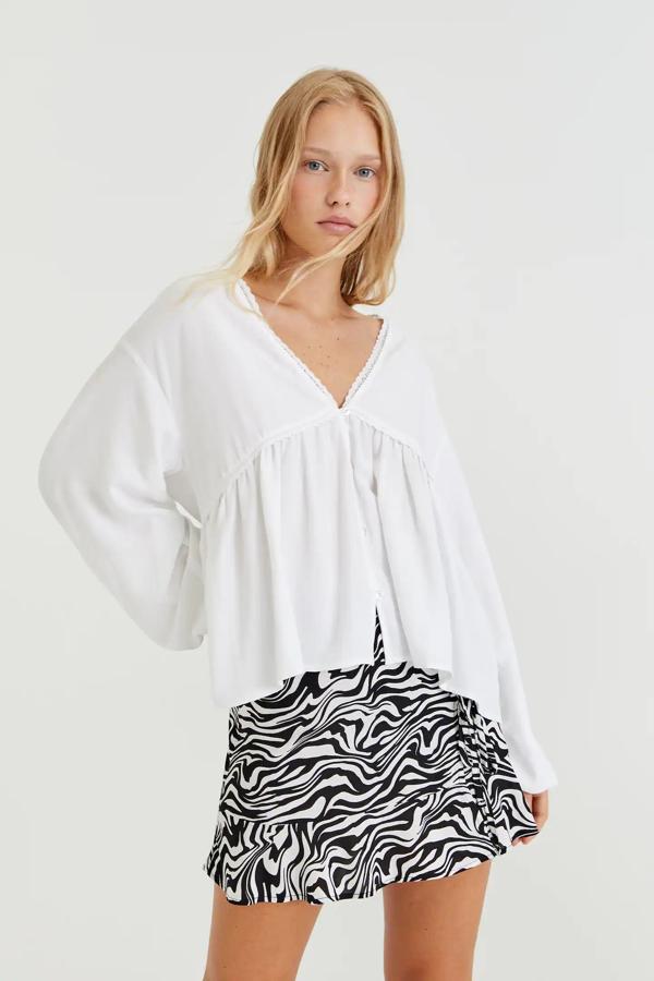 Con escote de pico y detalle de cintas y volantes, esta camisa de manga larga con botones delanteros es de Pull & Bear y tiene un precio de 22,99 euros.