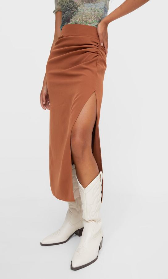 Disponible en negro, en marrón y en blanco, esta falda midi de Stradivarius con frunce lateral y bajo con abertura por encima de la rodilla tiene un precio de 22,99 euros y está disponible entre las tallas 34 y 44. 